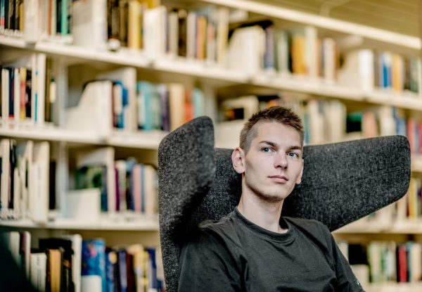 Ung mand sidder i en stol foran en reol med bøger